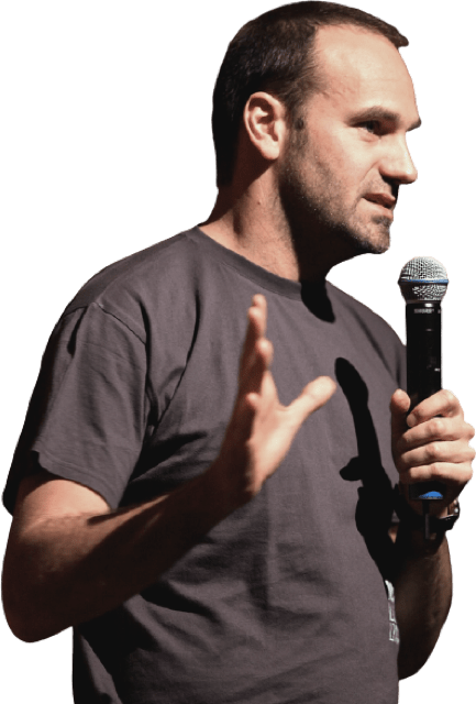  Mission specialist Mark Shuttleworth, a sideways standing guy with a black T-shirt and short brown hair, holding a microphone with one hand and holding the other hand open towards the person he is speaking to as if explaining something.